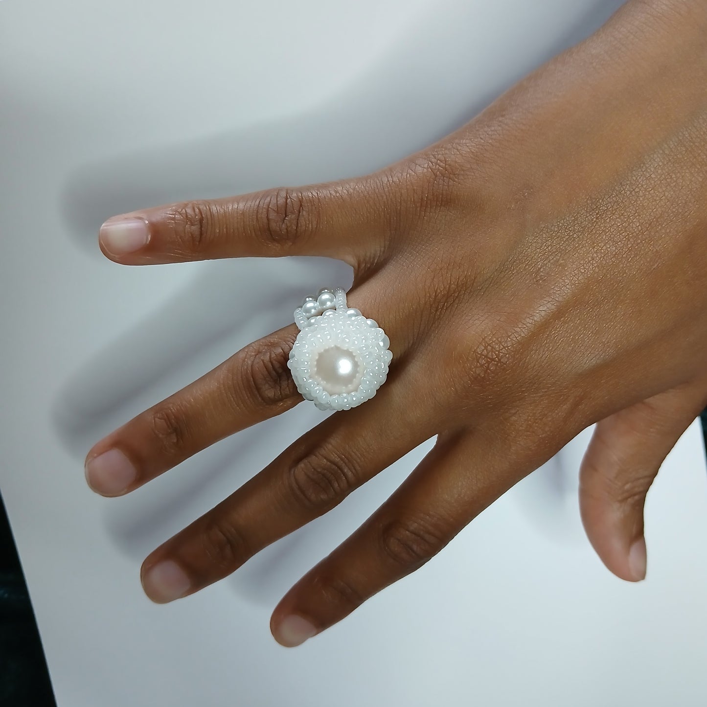 Hand wearing a decorative ring with a pearl on a plain background