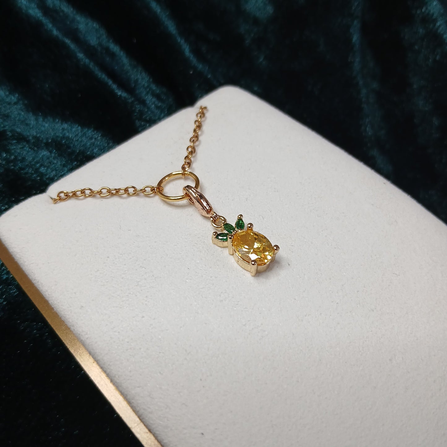 Gold bracelet with a yellow and green pineapple gemstone charm on a white cushion