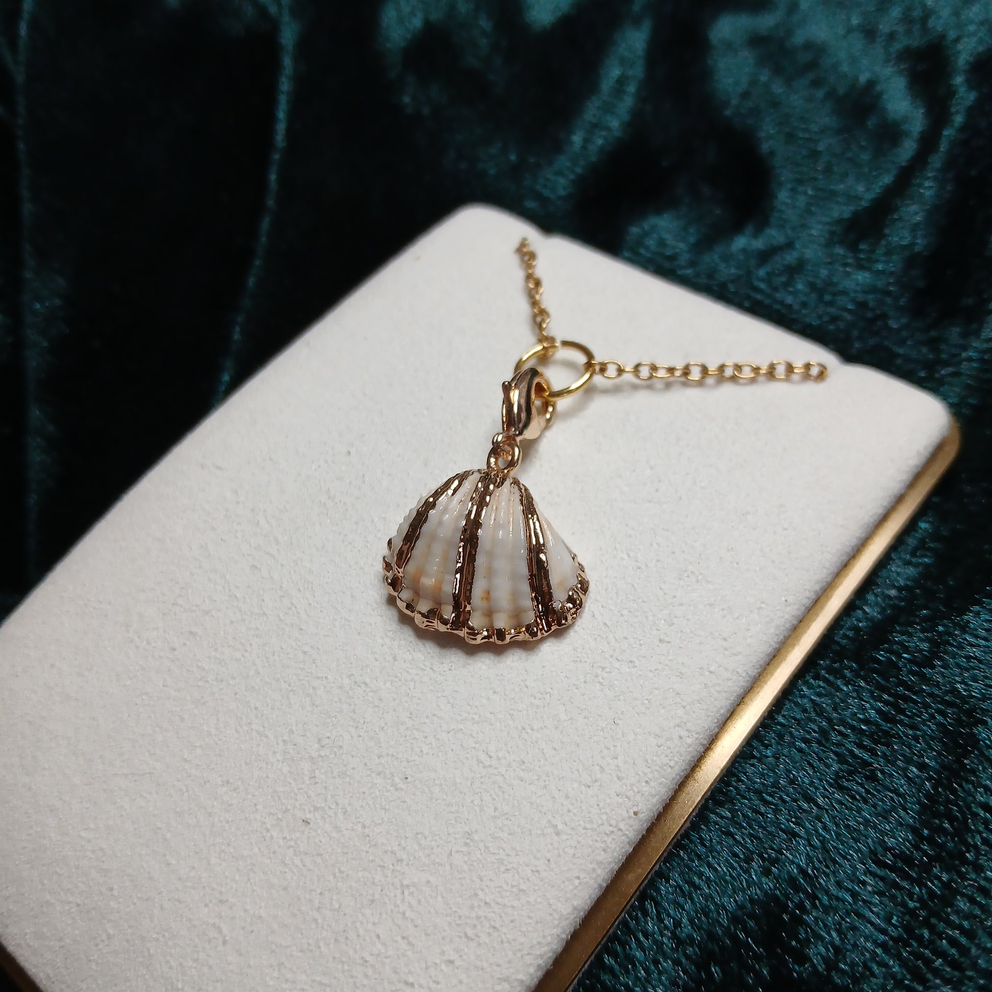 Gold foil shell pendant on a white cushion against a dark green velvet background